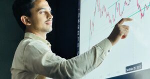 Man analyzing stock market graph on a digital board with a focused expression.